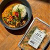 Bowl of Thai chicken curry with a container labeled 'Red Thai Chicken Curry' on a wooden surface